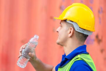 Ouvrier de chantier en casque de sécurité et gilet haute visibilité tenant une bouteille d’eau lors d’un épisode de forte chaleur