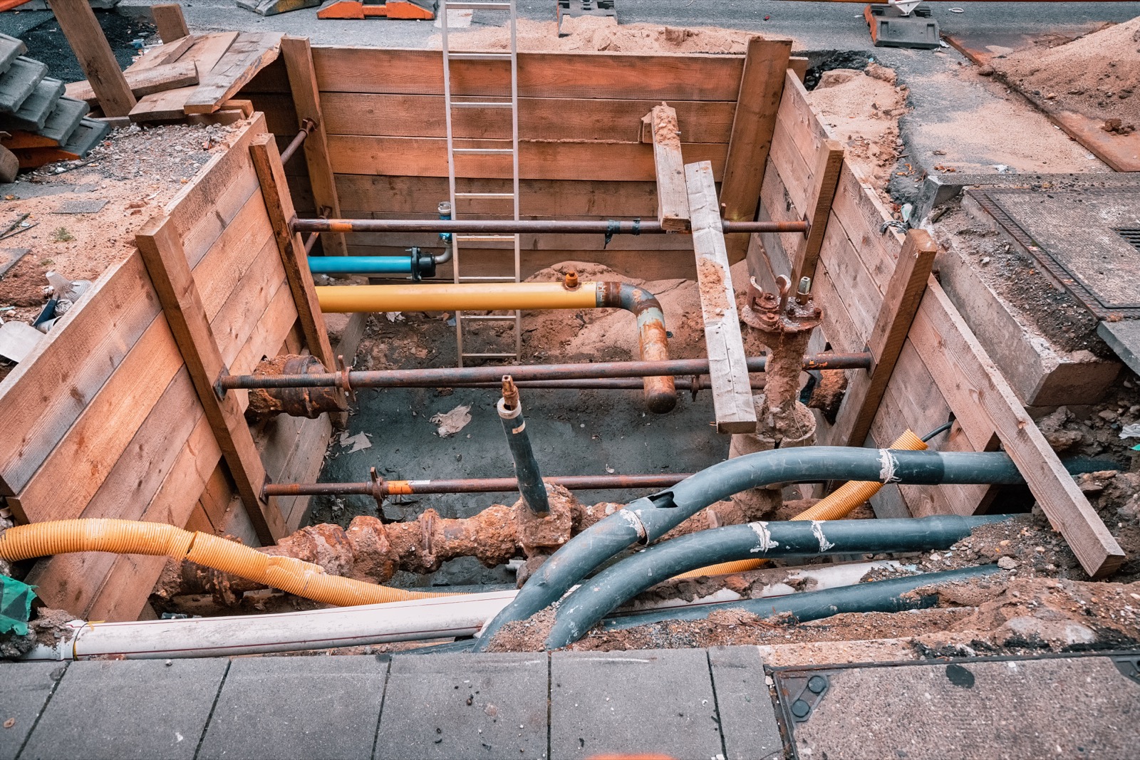 Tranchée blindée en rue laissant apparaître côte à côte des canalisations et des fourreaux de gaz, d’électricité et de télécommunications